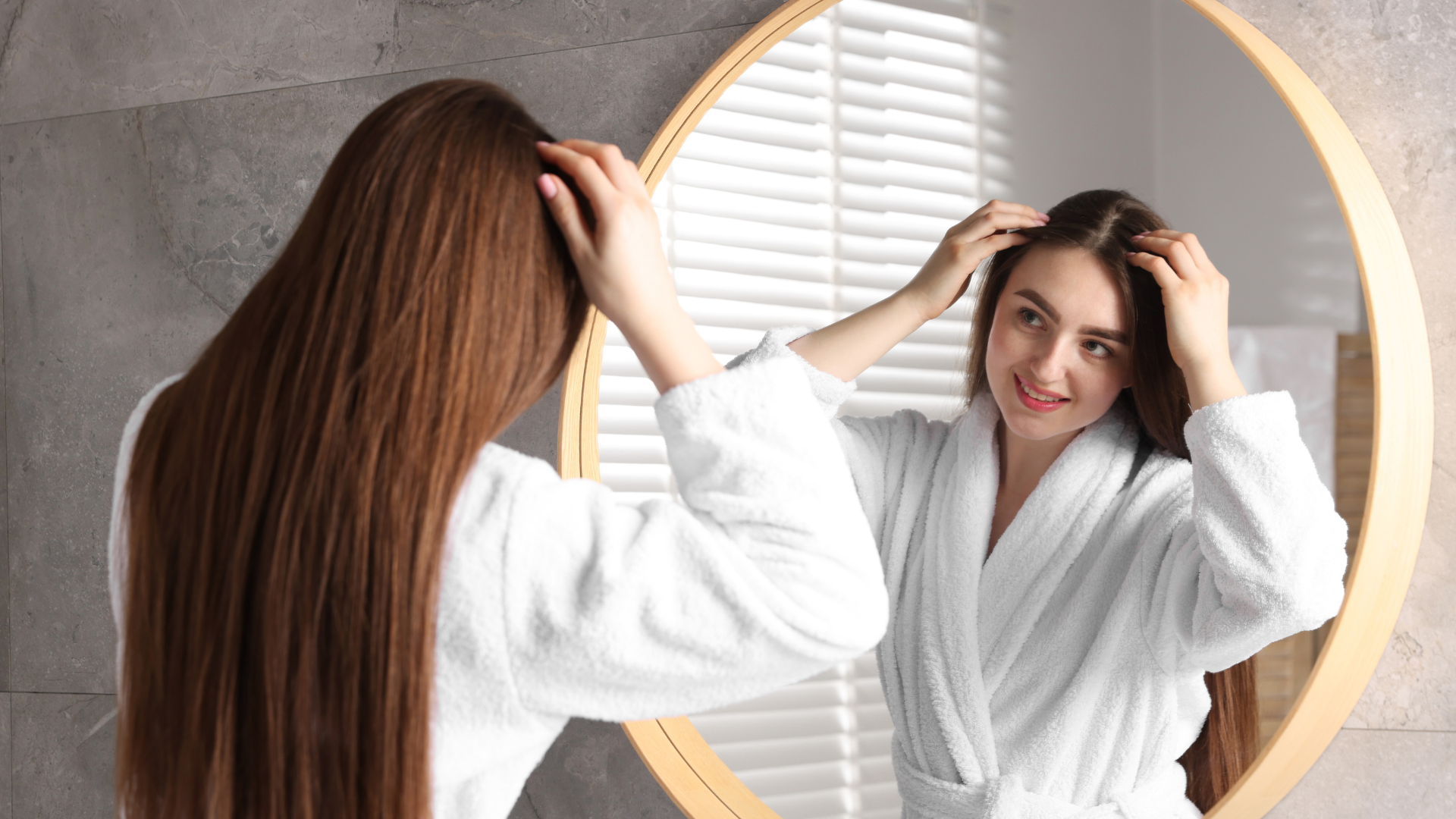 Woman checking her hairline in the mirror during postpartum hair regrowth.
