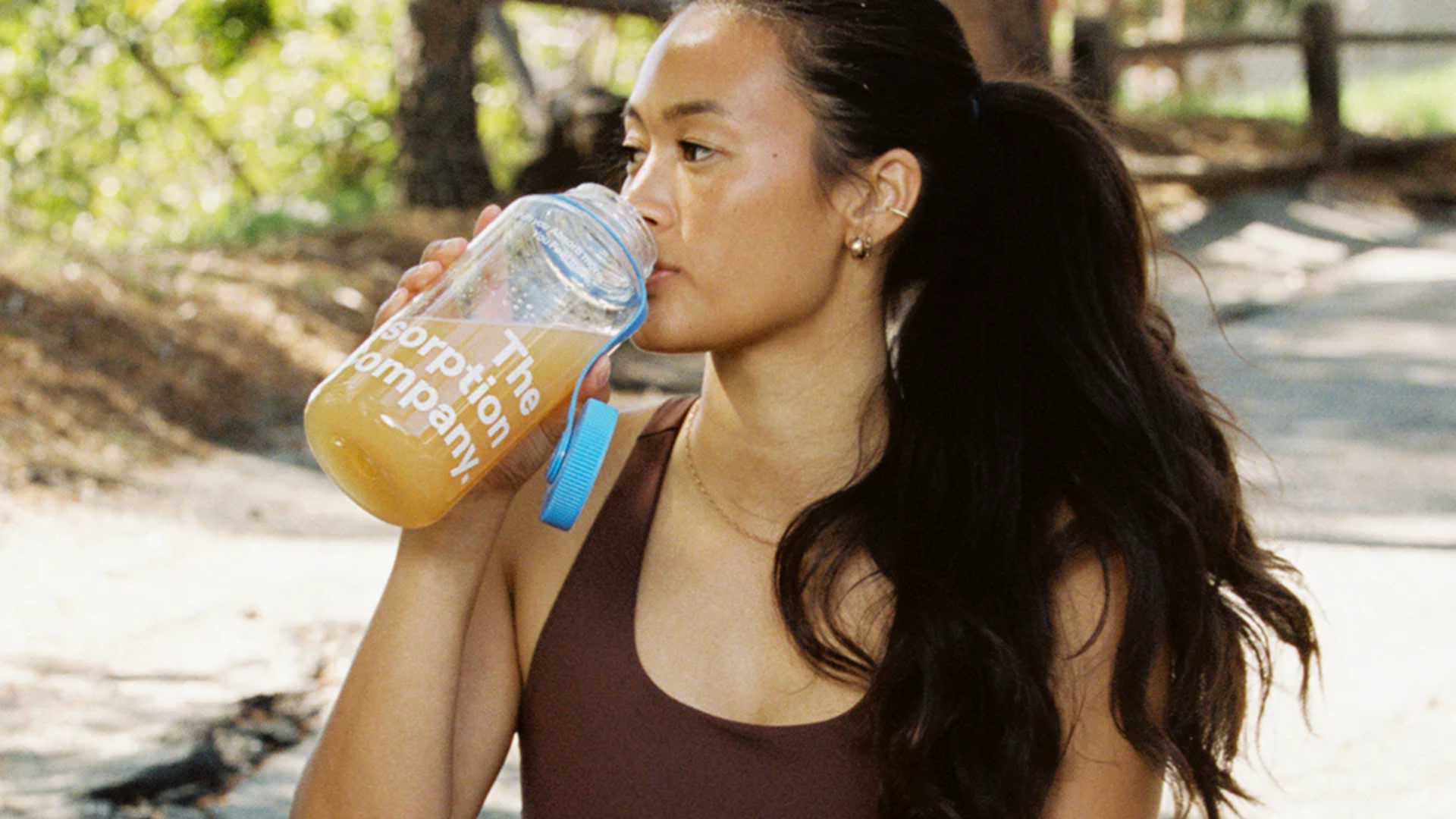 Woman drinking The Absorption Company supplement outdoors.